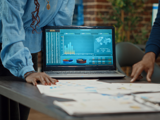 la imagen muestra a gente reunida en una mesa con un portátil abierto en una pantalla de datos financieros