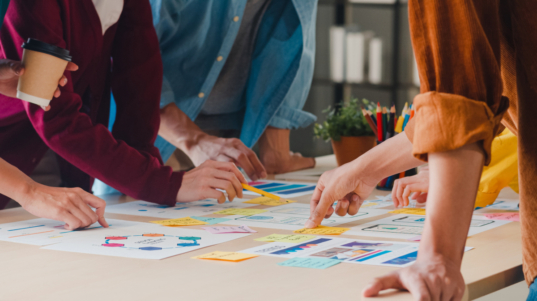 imagem mostra pessoas reunidas em torno de uma mesa de trabalho com anotações de insights estratégicos