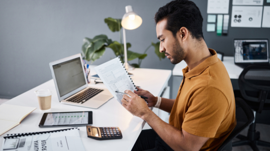imagem mostra um contador, profissional de finanças, sentado em sua mesa de trabalho analisando relatórios contábeis.