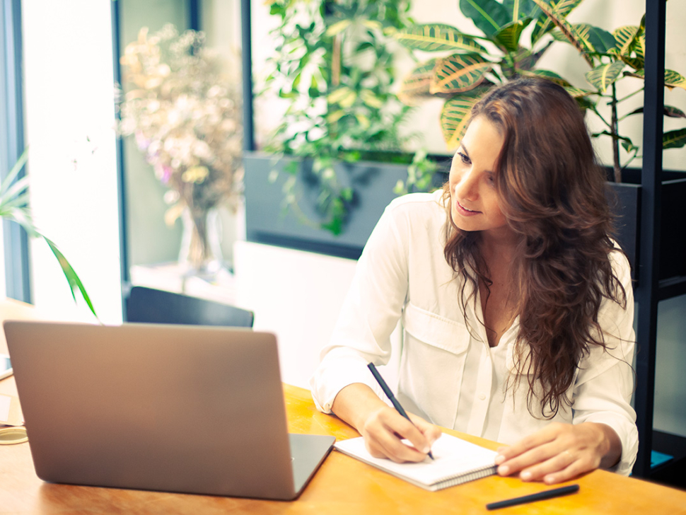 imagen muestra a una mujer satisfecha por haber hecho un cierre contable de éxito. Sobre su mesa, hay un cuaderno y un bloc de notas