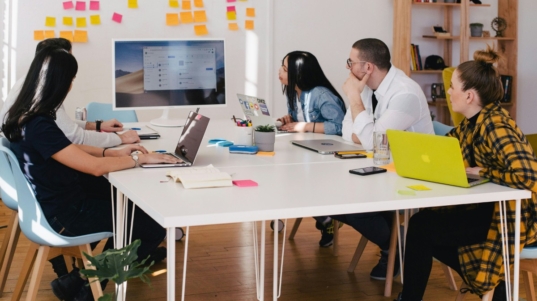 imagem mostra um grupo de colaboradores reunidos em uma mesa de escritório em uma reunião de gestão financeira empresarial