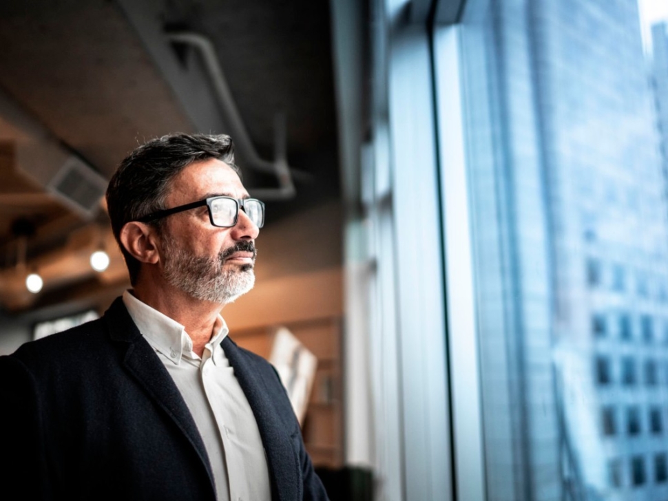 imagem mostra um homem de óculos olhando a janela de um prédio comercial