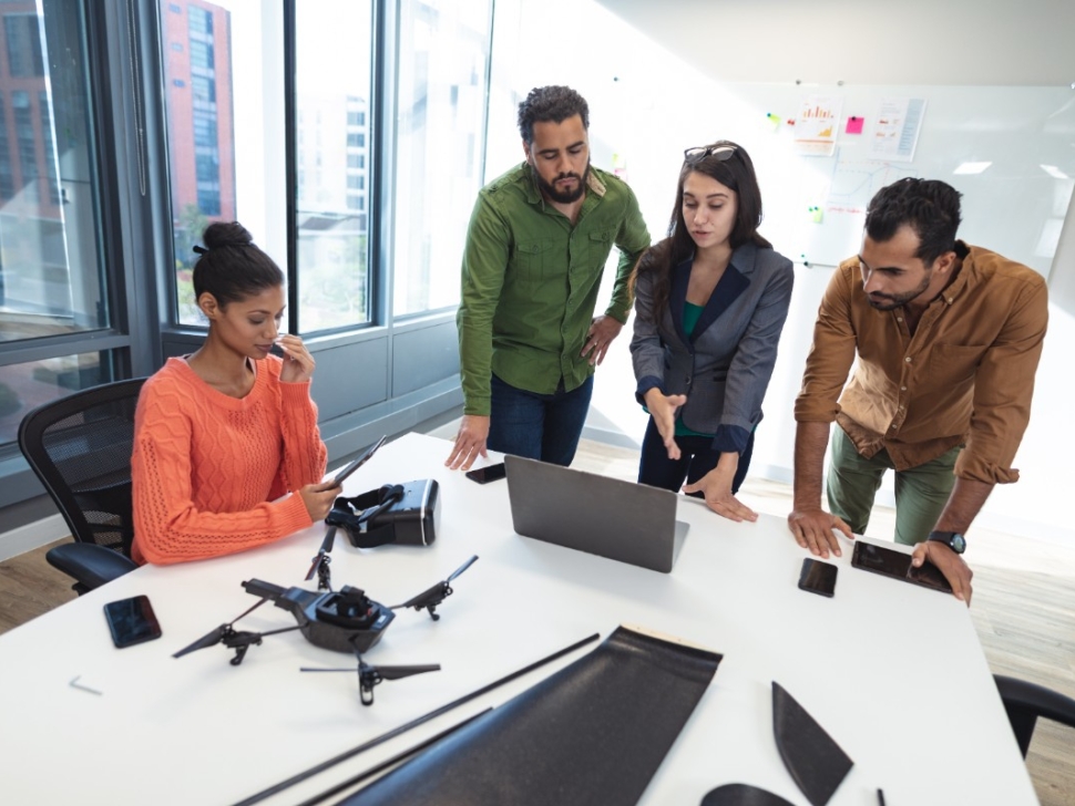 la imagen muestra a cuatro personas reunidas en una oficina frente a una pantalla portátil.