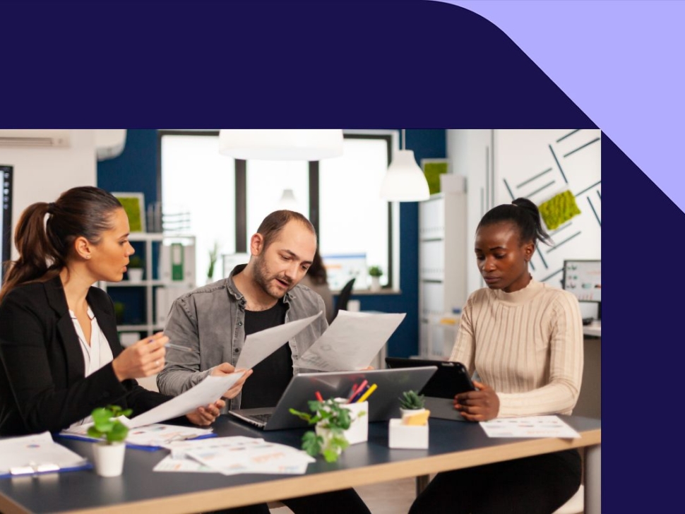 imagem mostra duas mulheres e um homem no escritório analisando documentos financeiros.